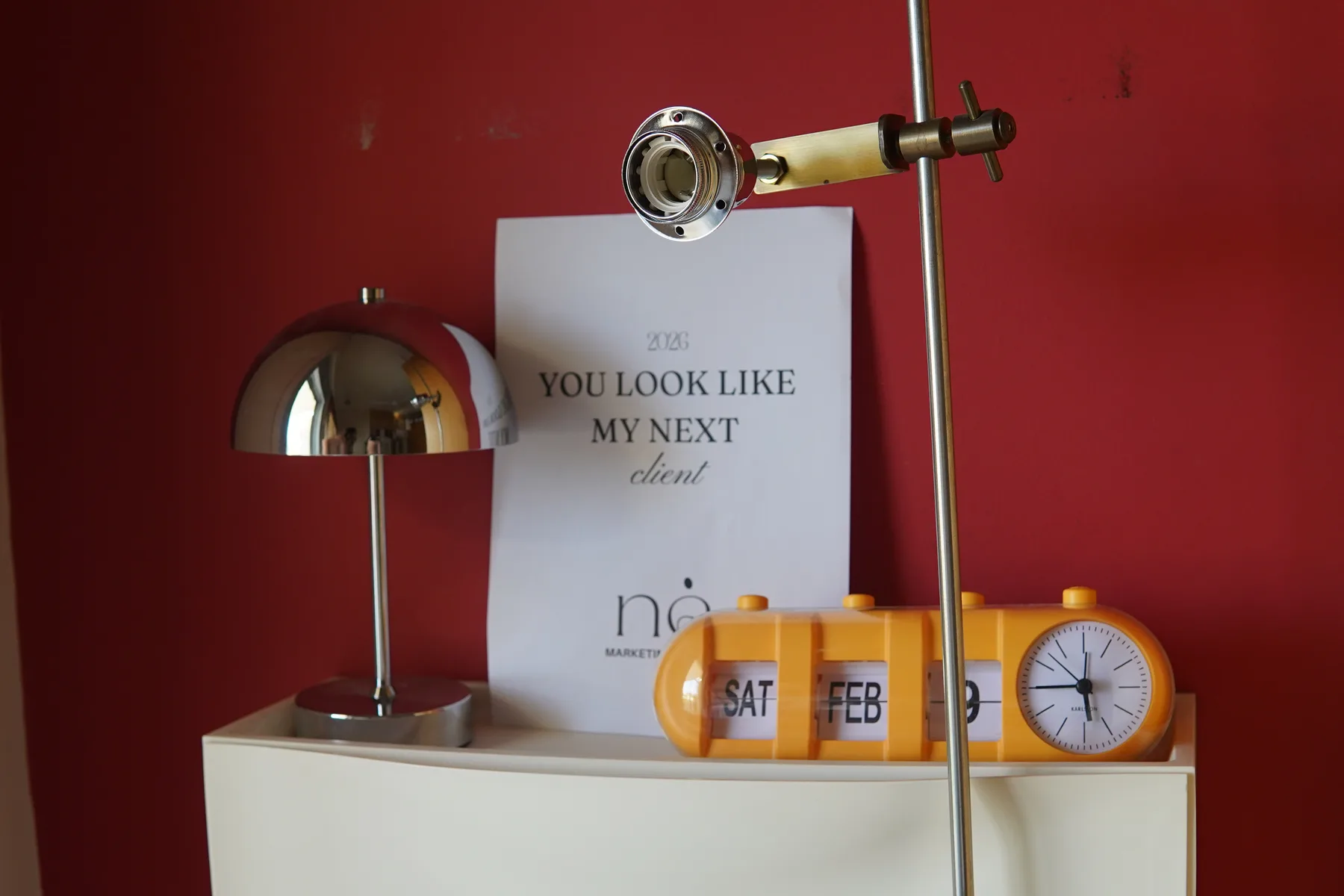 Styled editorial still life with a printed poster, desk lamp and orange flip clock